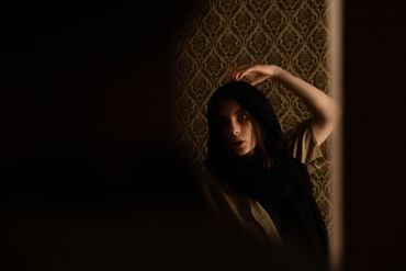 A woman looking at herself in the mirror as she removes a black fabric from her head