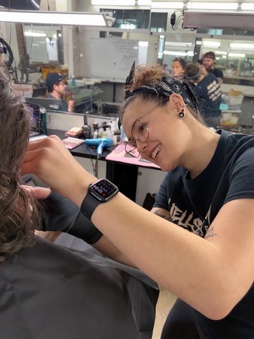 A photo of a Makeup Artist applying prosthetics to an Actor's face while he is sitting in the chair