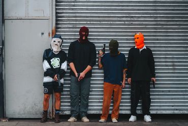 A group photo of men all wearing different masks and holding  guns standing in from of a garage door