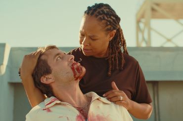 A woman standing behind a man holding his head and looking at him while his mouth is full of blood