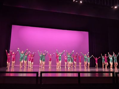 Children performing a colorful dance on stage with a purple backdrop.