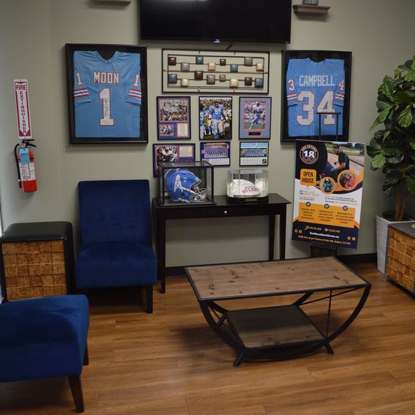 A sports-themed lounge with framed jerseys, sports memorabilia, and blue chairs.