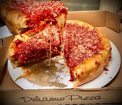 A slice of deep dish pizza with cheese stretching from the whole pizza and sauce covering the top.