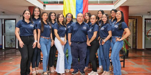 Group of people in navy blue shirts posing indoors with a Colombian flag.