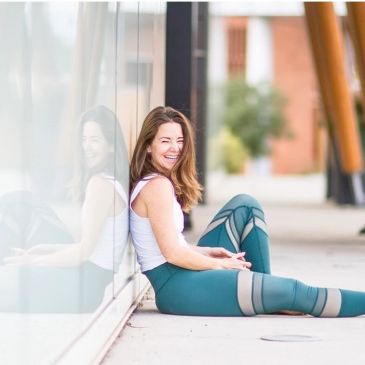 Woman in athletic wear sitting and smiling against glass wall.