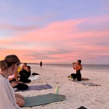 Group doing yoga on the beach at sunset with pink sky.