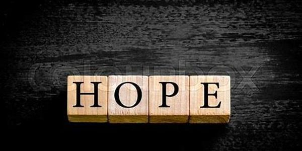Wooden blocks spell the word 'HOPE' on a dark surface.