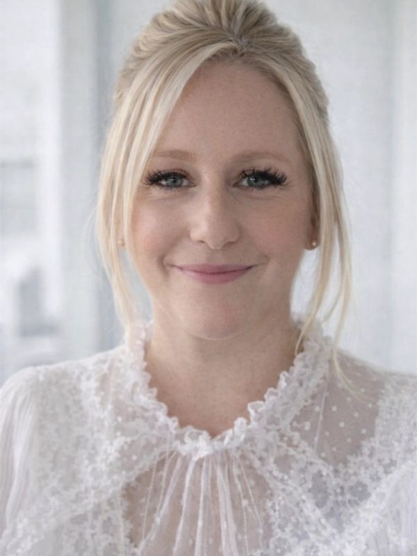 Smiling woman with blonde hair in a white lace blouse.