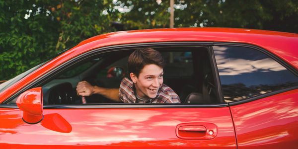 Young man smiling inside a red car, looking out the window.