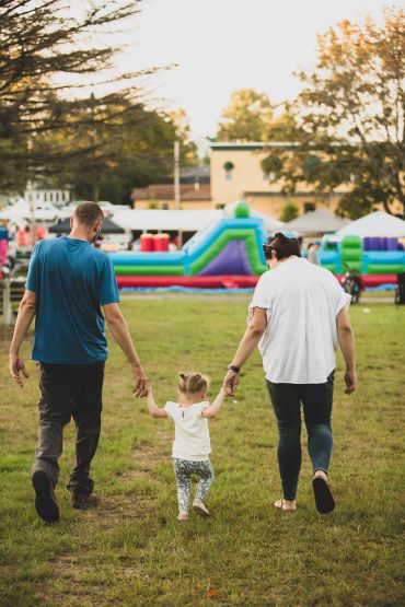 Parents holding hands with their child at a park.