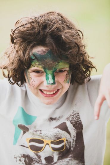 Child with face paint and curly hair smiling.