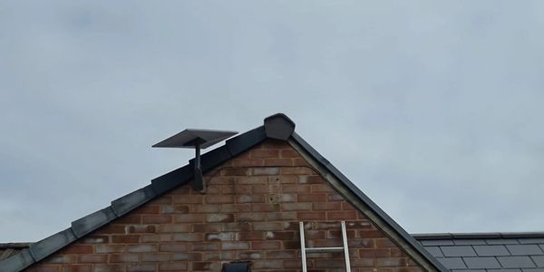 Brick house roof with a solar panel and a ladder against a cloudy sky.