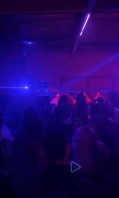 Dimly lit club scene with silhouettes and vibrant blue and purple lights.