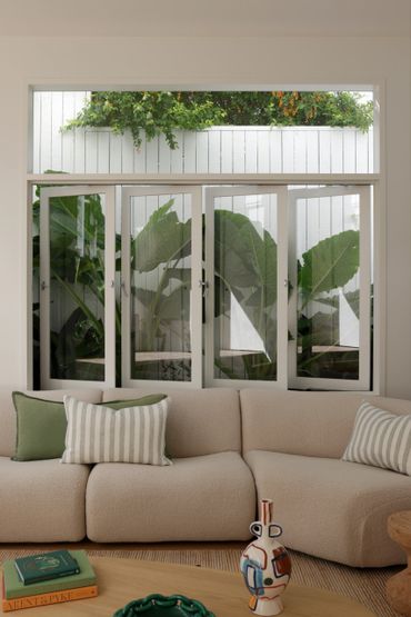 Cozy beige sofa with green and striped pillows by a window showing lush greenery outside.