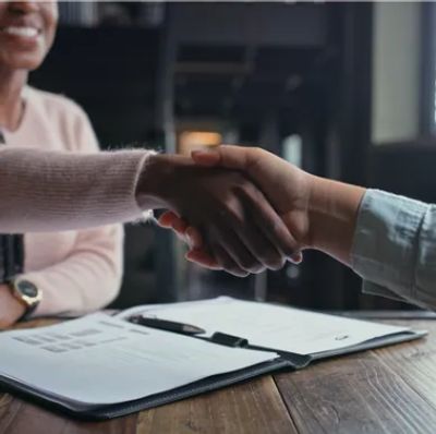 Two people shaking hands over a table with documents and a pen.