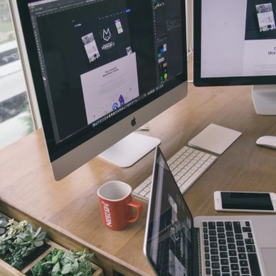 Workspace with desktop and laptop showing design software, a red coffee mug, and a smartphone.