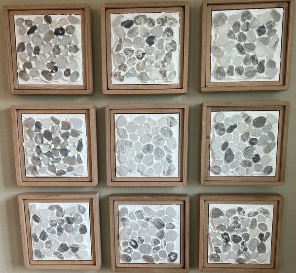 Nine squares of wooden framed plaster with flat grey stones embedded into each frame