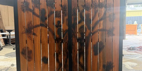 Wooden gate with a tree and leaf design carved and painted in black.