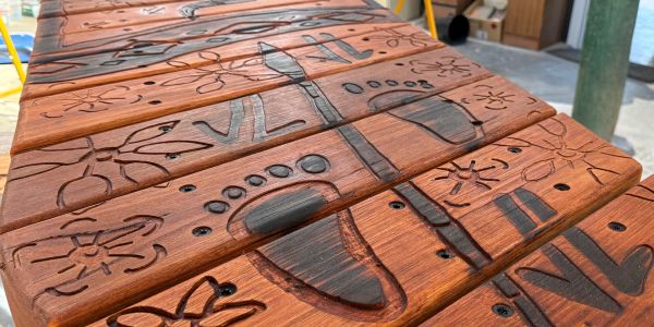 Close-up of a wooden table with carved airplane and flower designs.