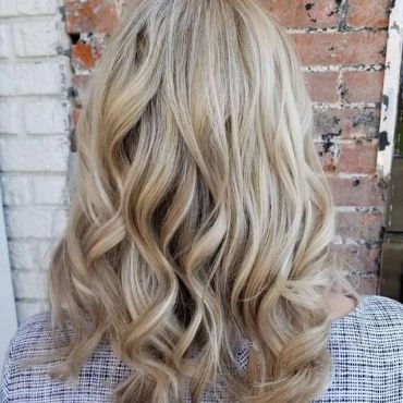 Curly blonde hair from behind against a brick wall.
