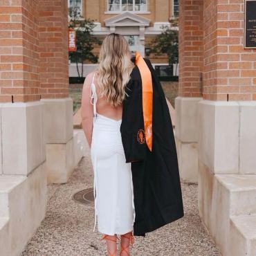 Woman in white dress holding graduation gown outdoors.