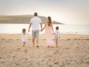 beach image of family holding hand facing away from the camera wearing pastel and white colours.