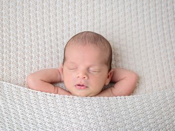 sleeping newborn with his arms behind his head 