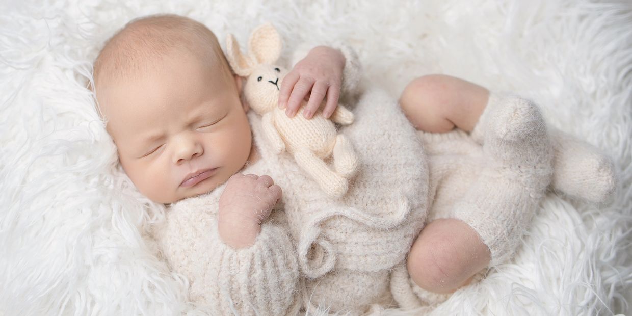 Sleeping baby in knitted outfit holding a small stuffed bunny.