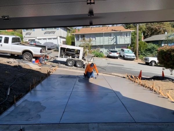 Worker smoothing freshly poured concrete driveway in a residential area.