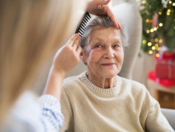 A health visitor combing hair of senior woman at home at Christmas time.