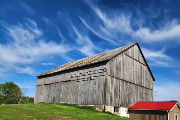 Old wooden barn under a bright blue sky with wispy clouds.