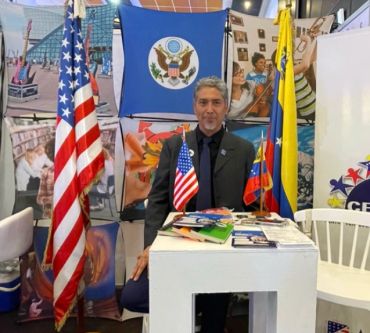 Hombre detrás de mesa con banderas de EE.UU. y Venezuela.