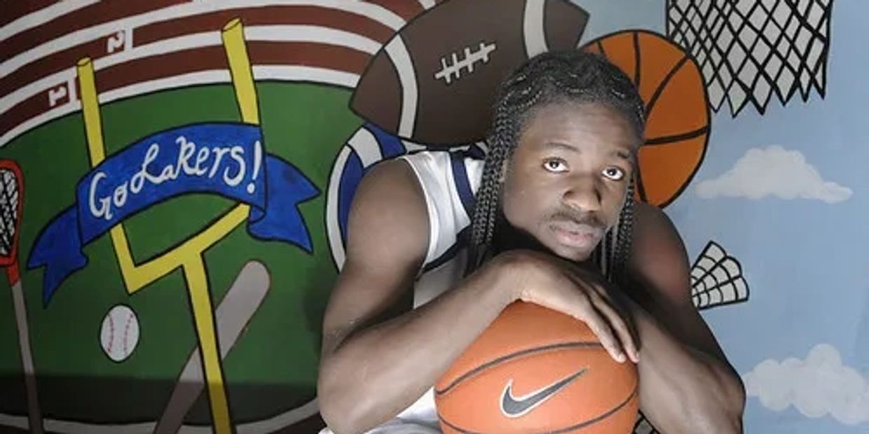Young man with braided hair holding a basketball, with sports-themed mural background.