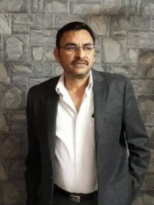 Man in a suit and glasses standing against a stone wall.