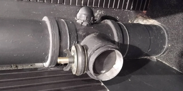 Close-up of a black pipe joint with a valve and bolt in an industrial setting.