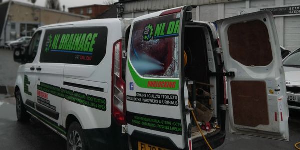 A white van with open back doors displaying drainage service advertisements.
