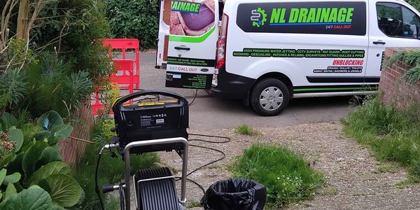 Service vans and equipment for NL Drainage in a residential garden.