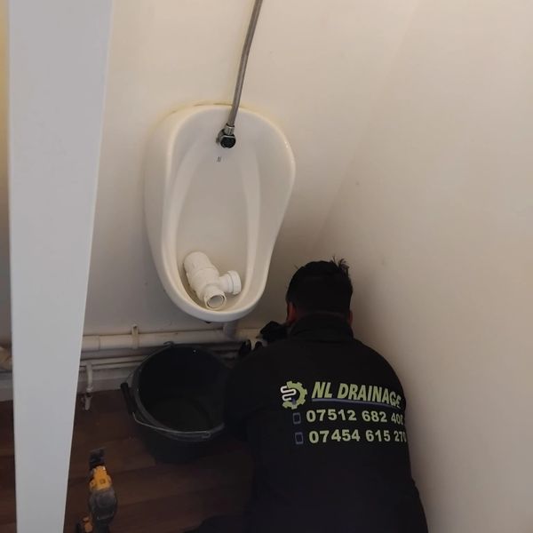 A plumber fixing a urinal in a small restroom corner.