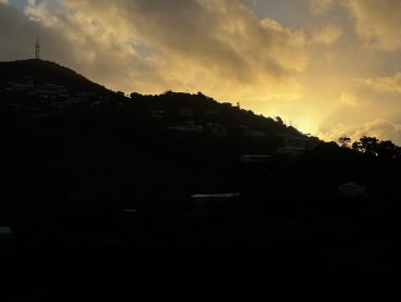 Sunset behind a silhouetted hillside with scattered houses and trees.