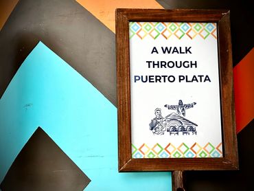 Signboard reading 'A Walk Through Puerto Plata' with colorful geometric border.