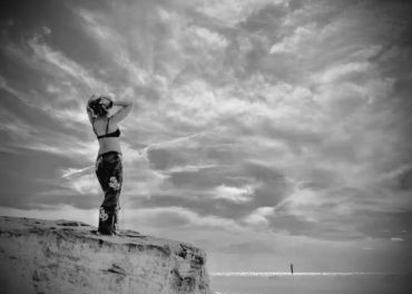 A woman stands on a cliff, gazing at the sky in a black-and-white photo.