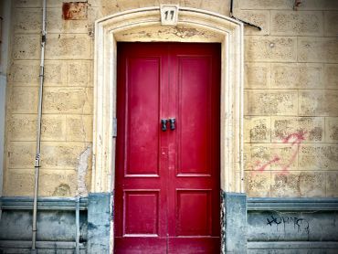 A vivid red door with double panels set in a stone wall under number 11.