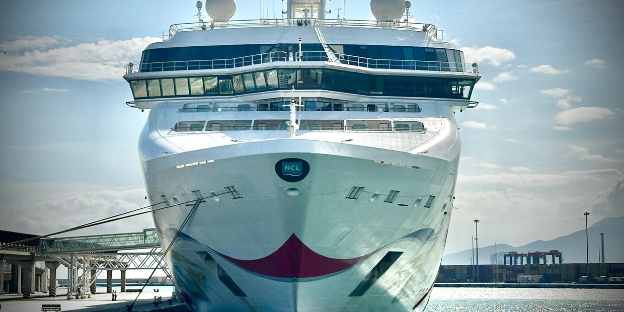 Front view of a large cruise ship docked at a port on a sunny day.