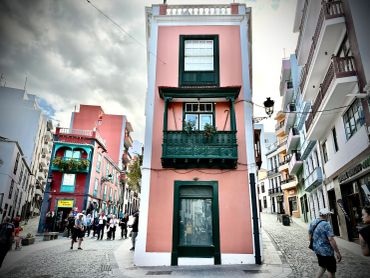 Narrow pink building with green accents on a lively street.