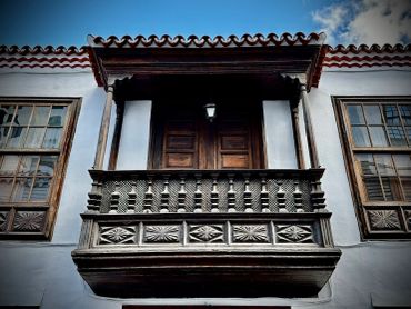 Ornate wooden balcony on a traditional building under a blue sky.