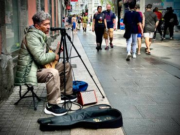 Street musician playing guitar with an open case for tips on a busy sidewalk.