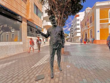 Statue of a man in uniform holding a book in a pedestrian street.