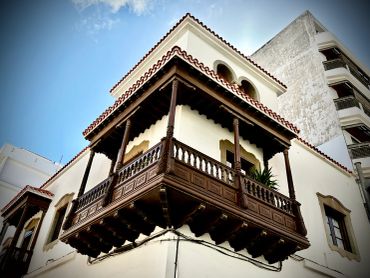 Ornate wooden balcony on a white building under a blue sky.