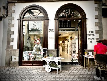 Charming storefront of The Shell Room with decorative items and a customer outside.