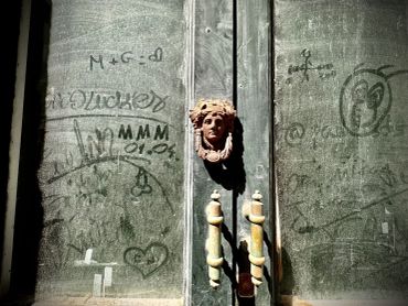Antique door with a carved face handle and graffiti marks.